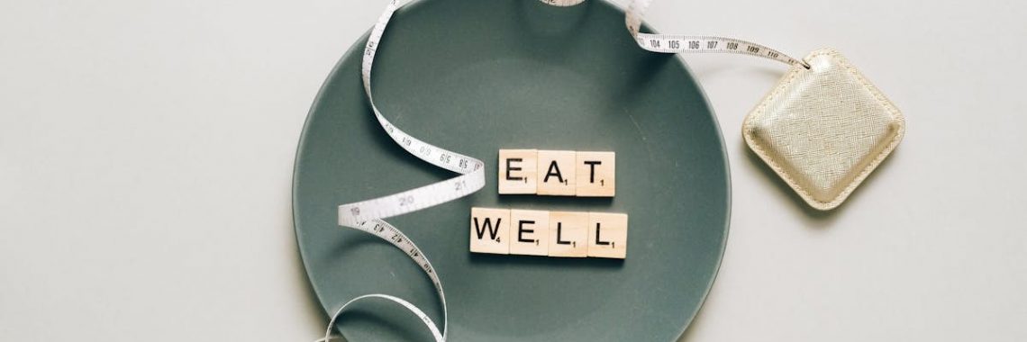 Flat lay of scrabble tiles spelling 'eat well' on a plate with a tape measure, promoting healthy eating.